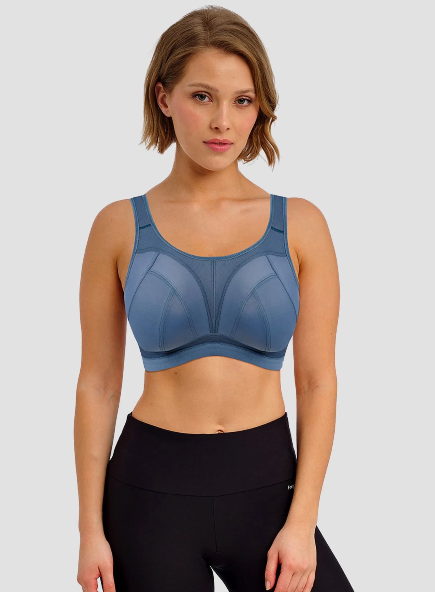 Woman wearing a blue sports bra and black leggings on a light gray background