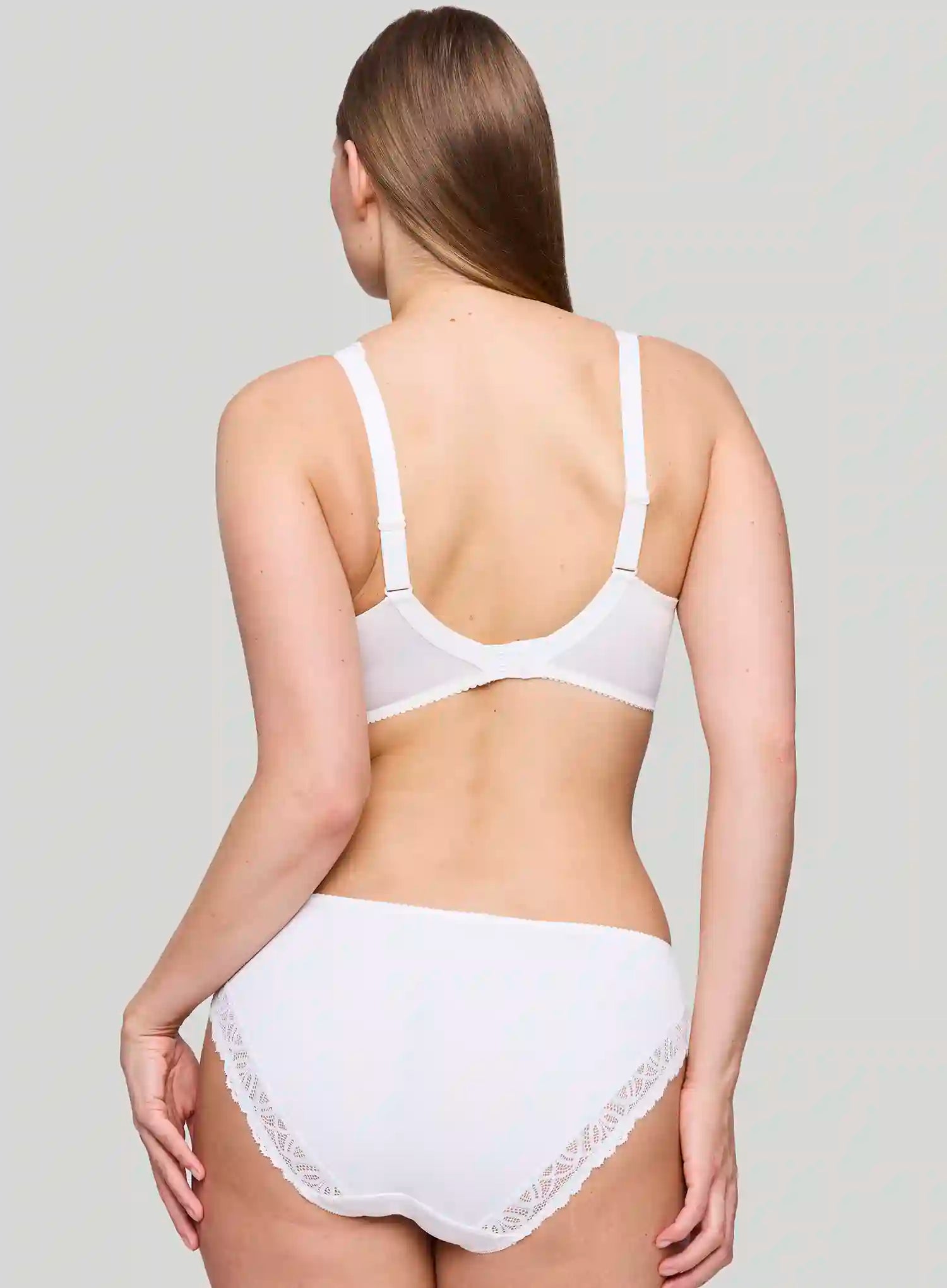 Woman wearing a white bra and underwear set against a plain background