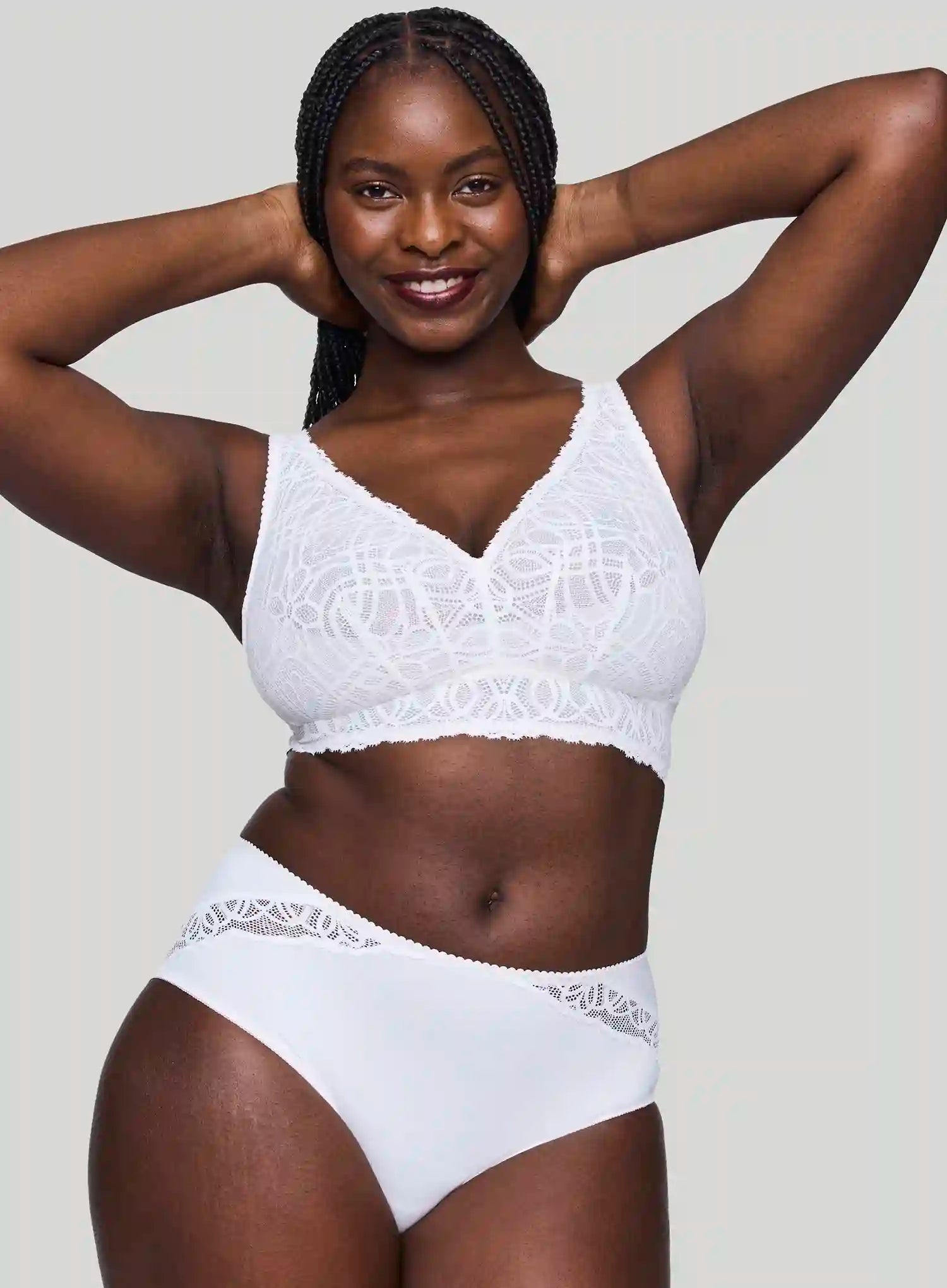 Woman wearing a white lace lingerie set against a plain background