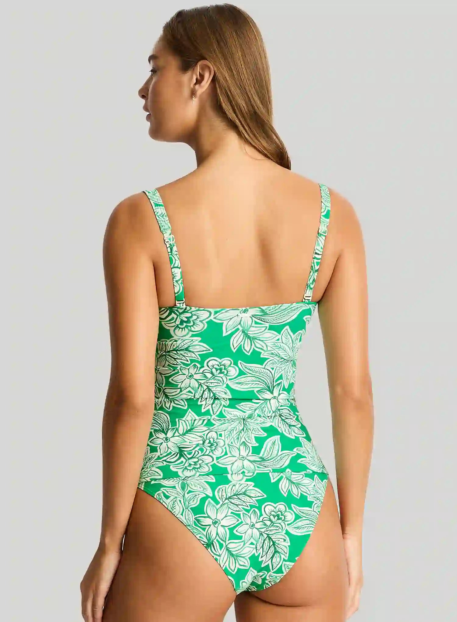 Woman wearing a green floral one-piece swimsuit on a gray background