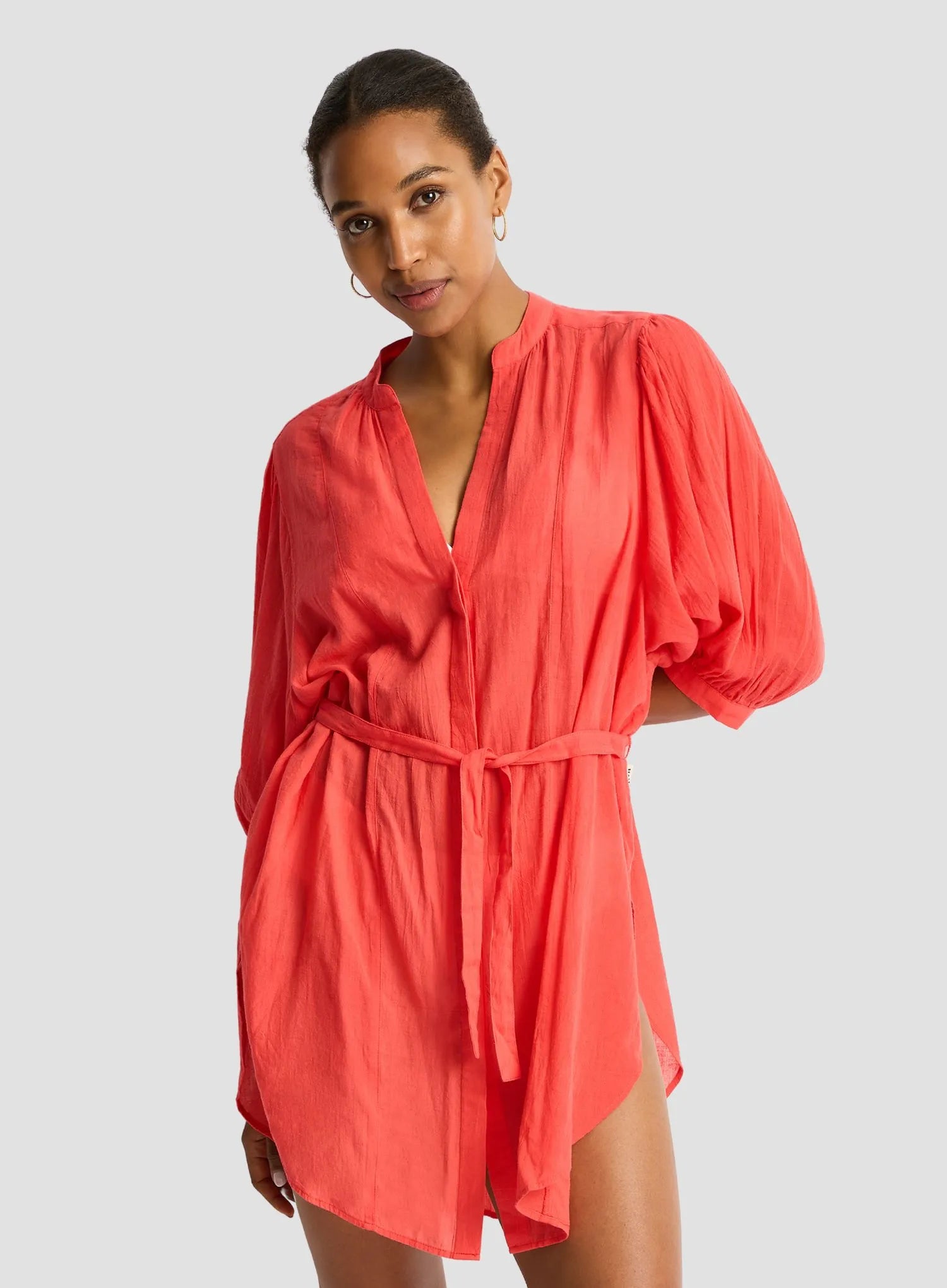 Woman wearing a coral dress with puff sleeves on a gray background