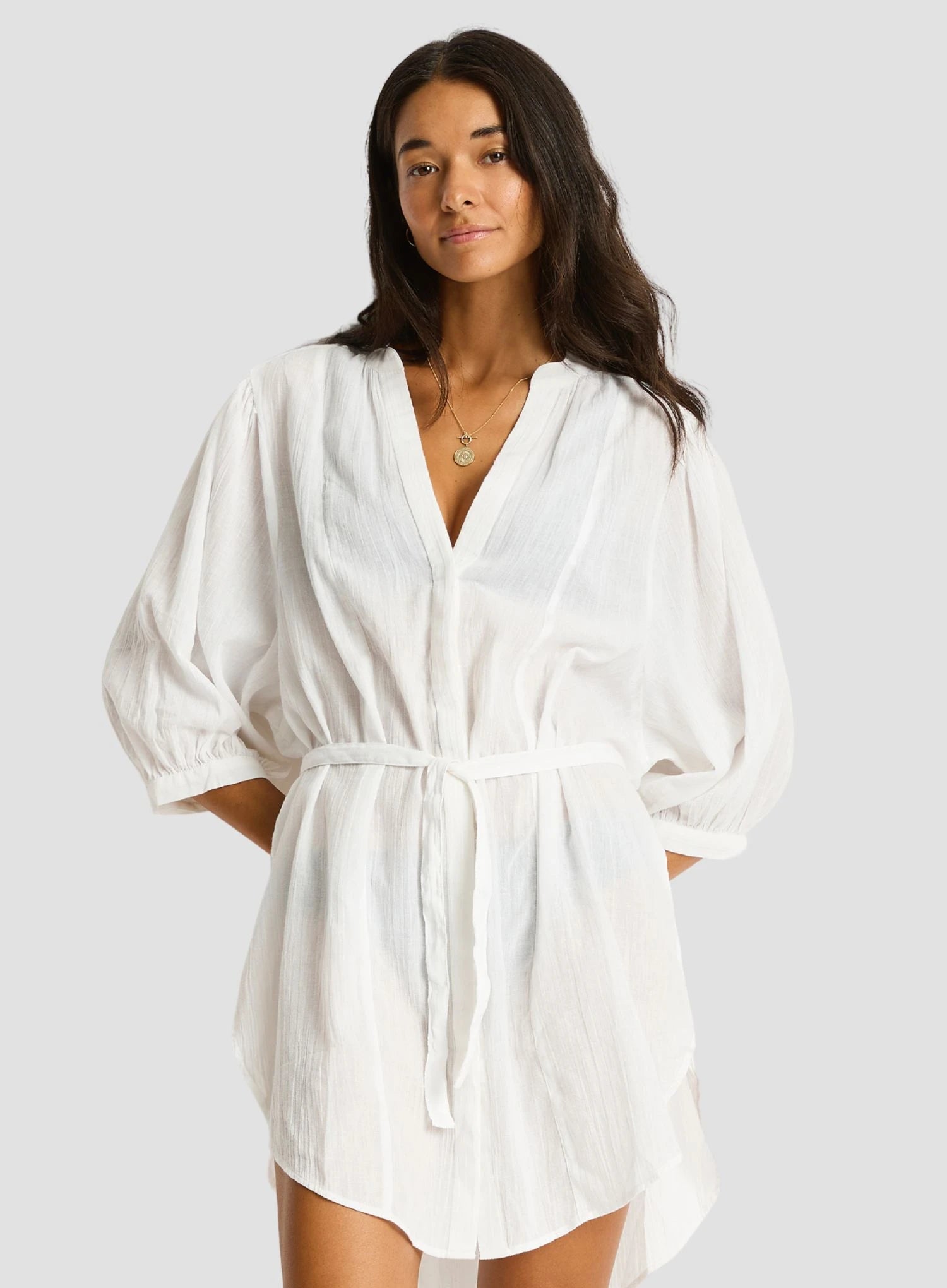 Woman wearing a white cover-up dress against a plain background